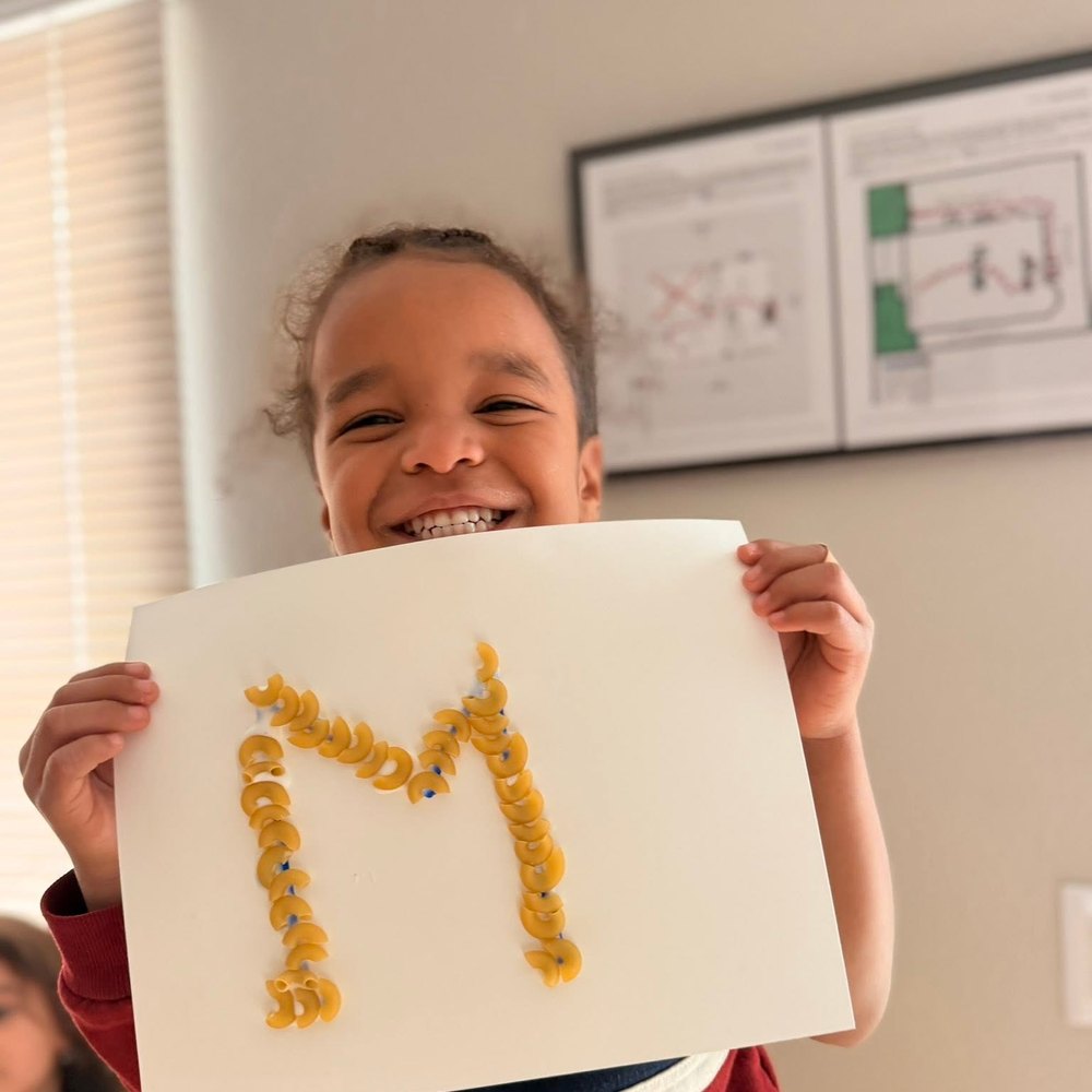 Child holding up a letter M made from pasta art